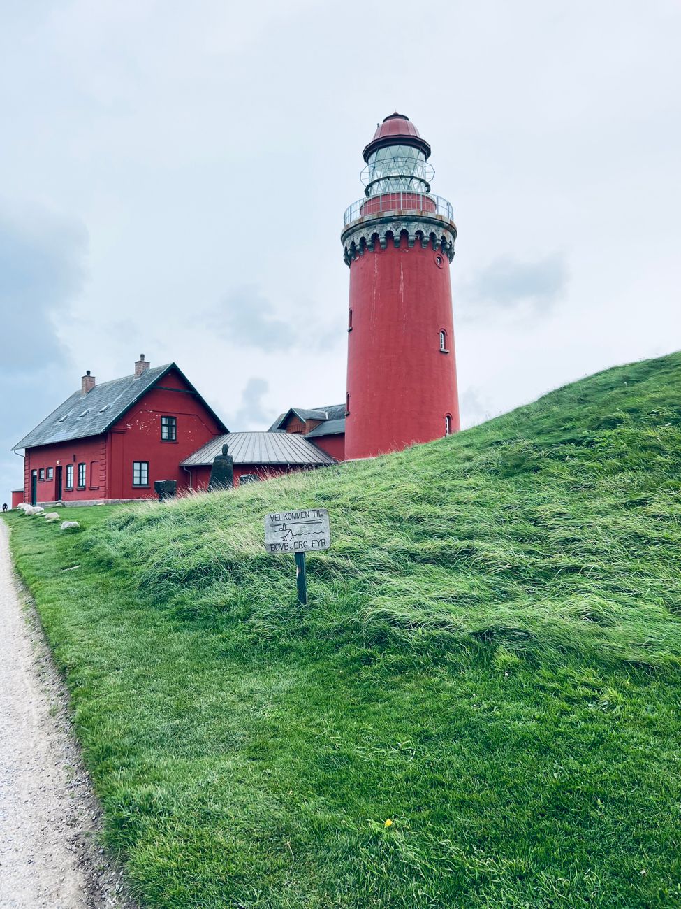 Et rødt fyrtårn og røde bygninger på en grøn skråning under en grå himmel